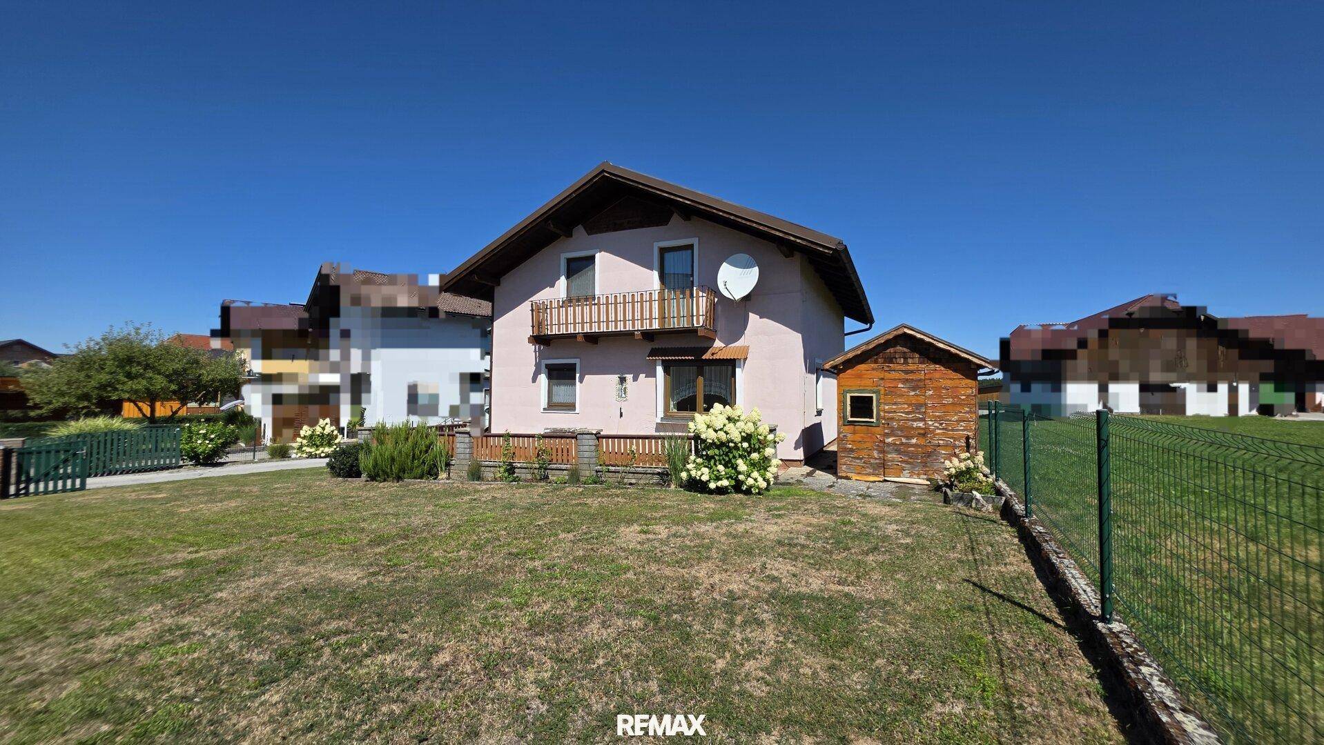 Vorderansicht des Einfamilienhauses mit Balkon und kleinem Gartenhaus.