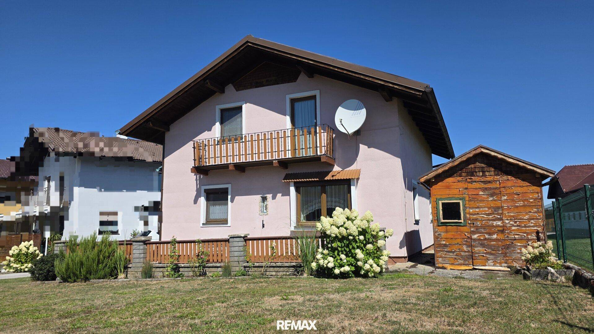 Vorderansicht des Einfamilienhauses mit Balkon und Gartenhaus bei Sonnenschein.