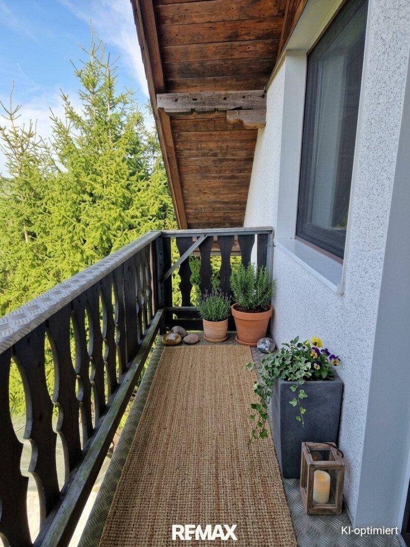 Kleiner Balkon mit traditionellem Holzgeländer, Pflanzen und Blick ins Grüne.