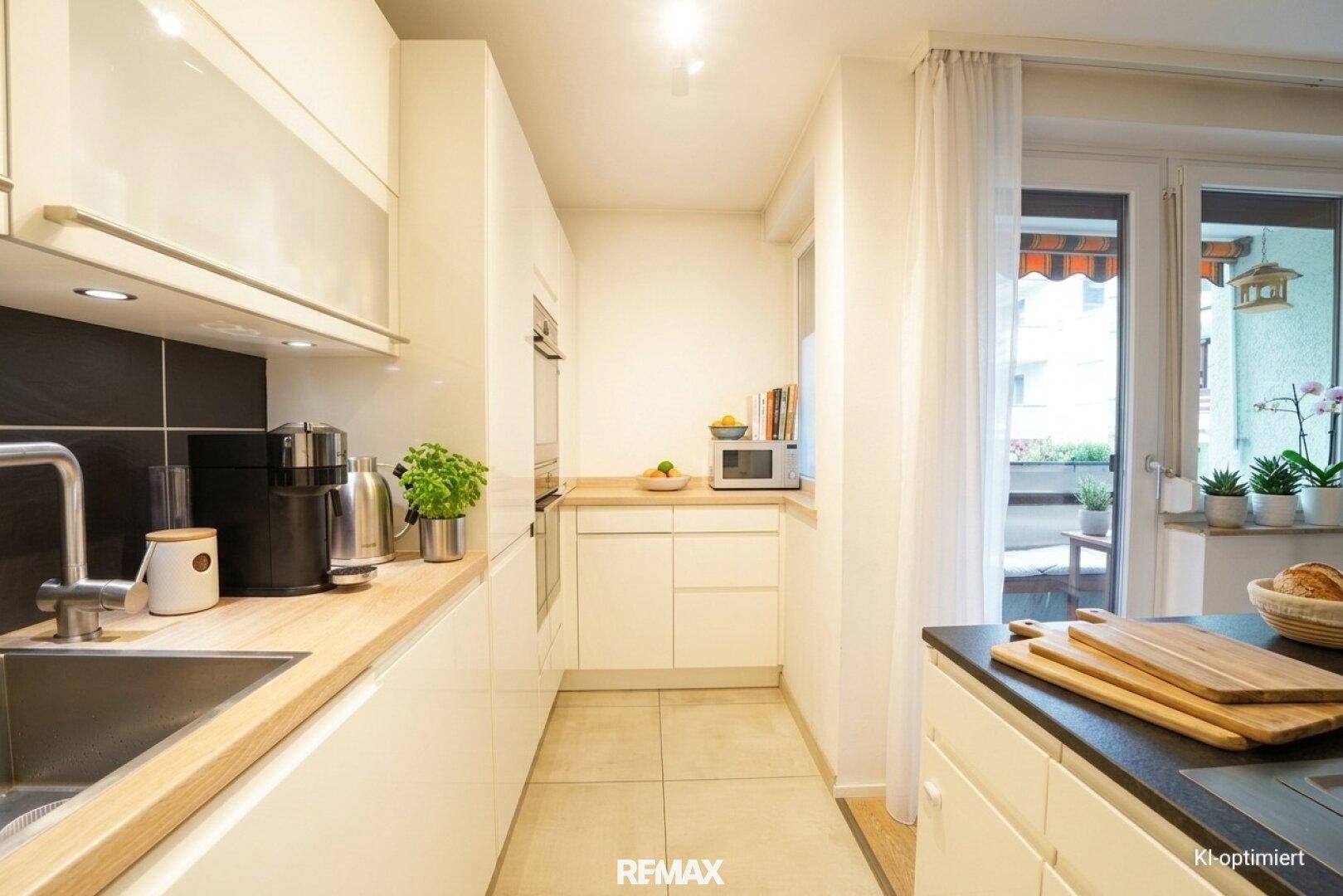 Moderne Küche mit hellen Schränken, Holzarbeitsplatte und Zugang zum sonnigen Balkon.