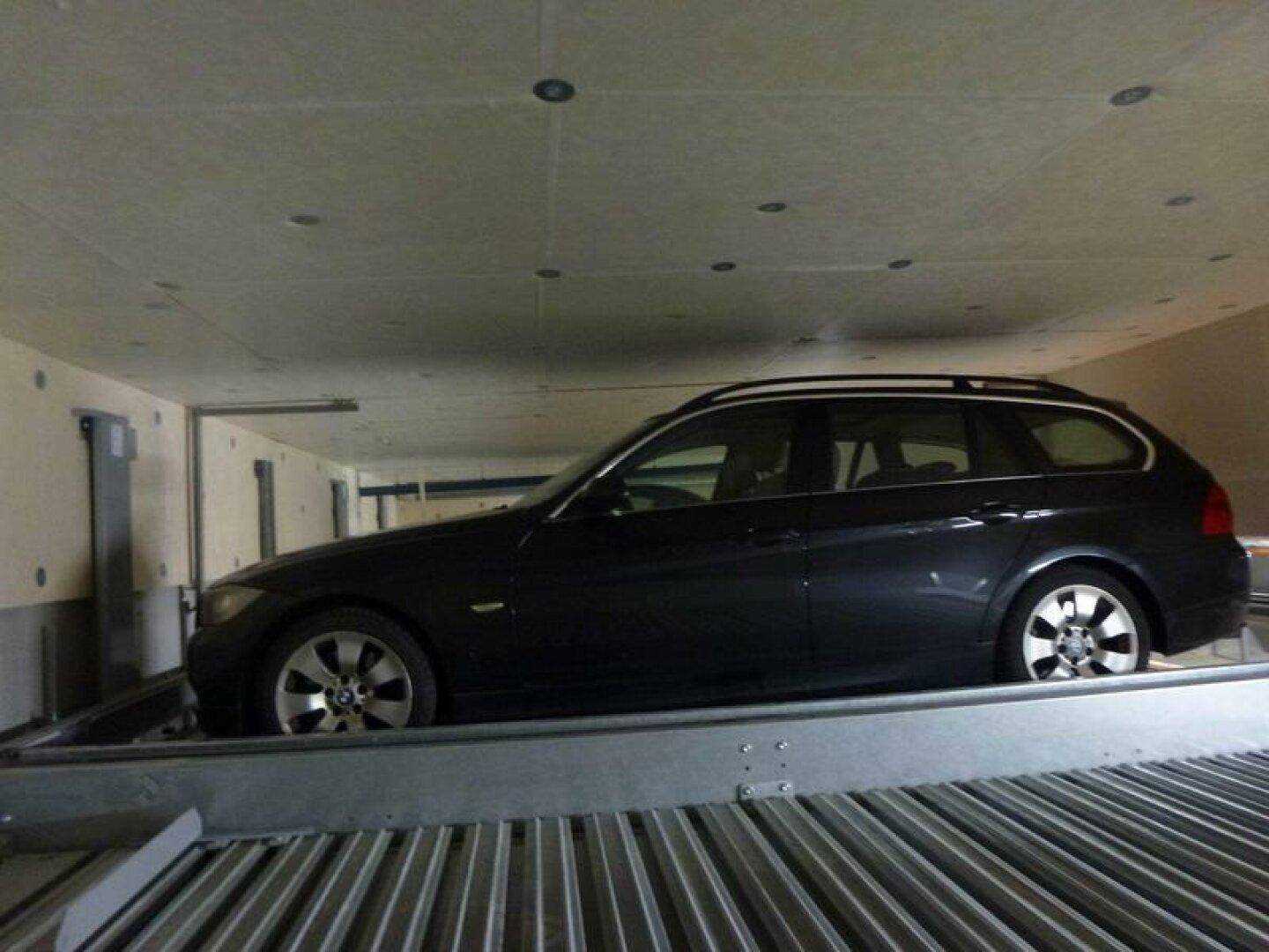 Ein schwarzer Kombi parkt auf einer Hebebühne eines automatischen Parksystems in der Tiefgarage.
