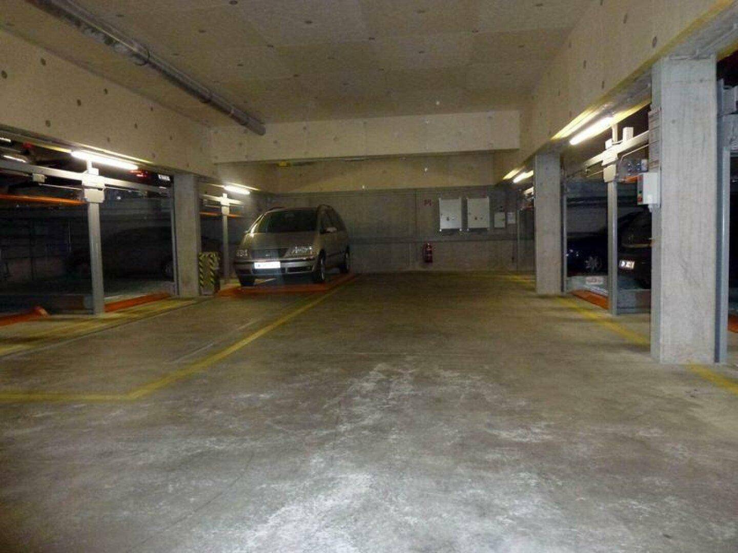 Geräumige Tiefgarage mit mehreren automatischen Parksystemen und einem geparkten Fahrzeug auf dem Betonboden.