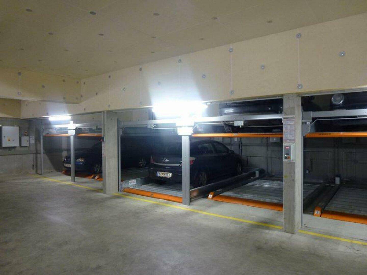 Reihe von automatischen Parksystemen in einer modernen Tiefgarage mit mehreren Fahrzeugen und heller Beleuchtung.