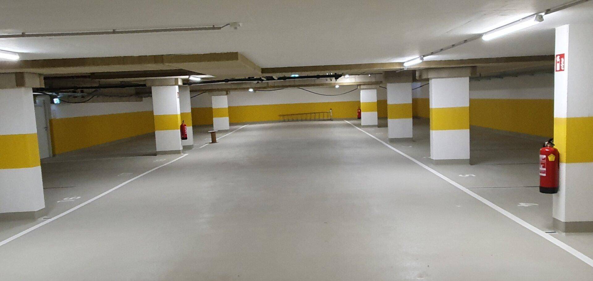 Tiefgarage mit markierten Stellplätzen, gelb-weißen Säulen und Feuerlöschern, gut beleuchtet.