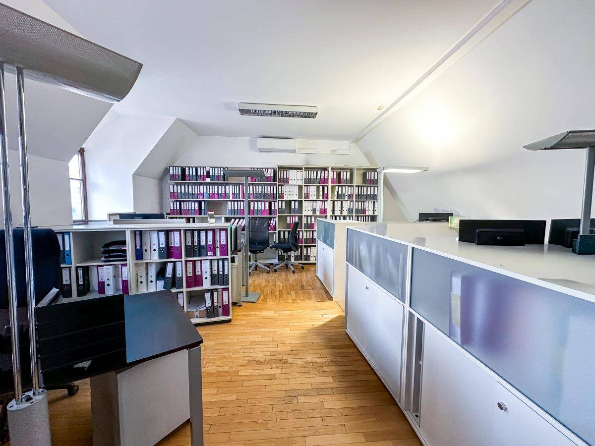 Großes Großraumbüro mit Dachschrägen, vielen Aktenregalen und mehreren Arbeitsplätzen.