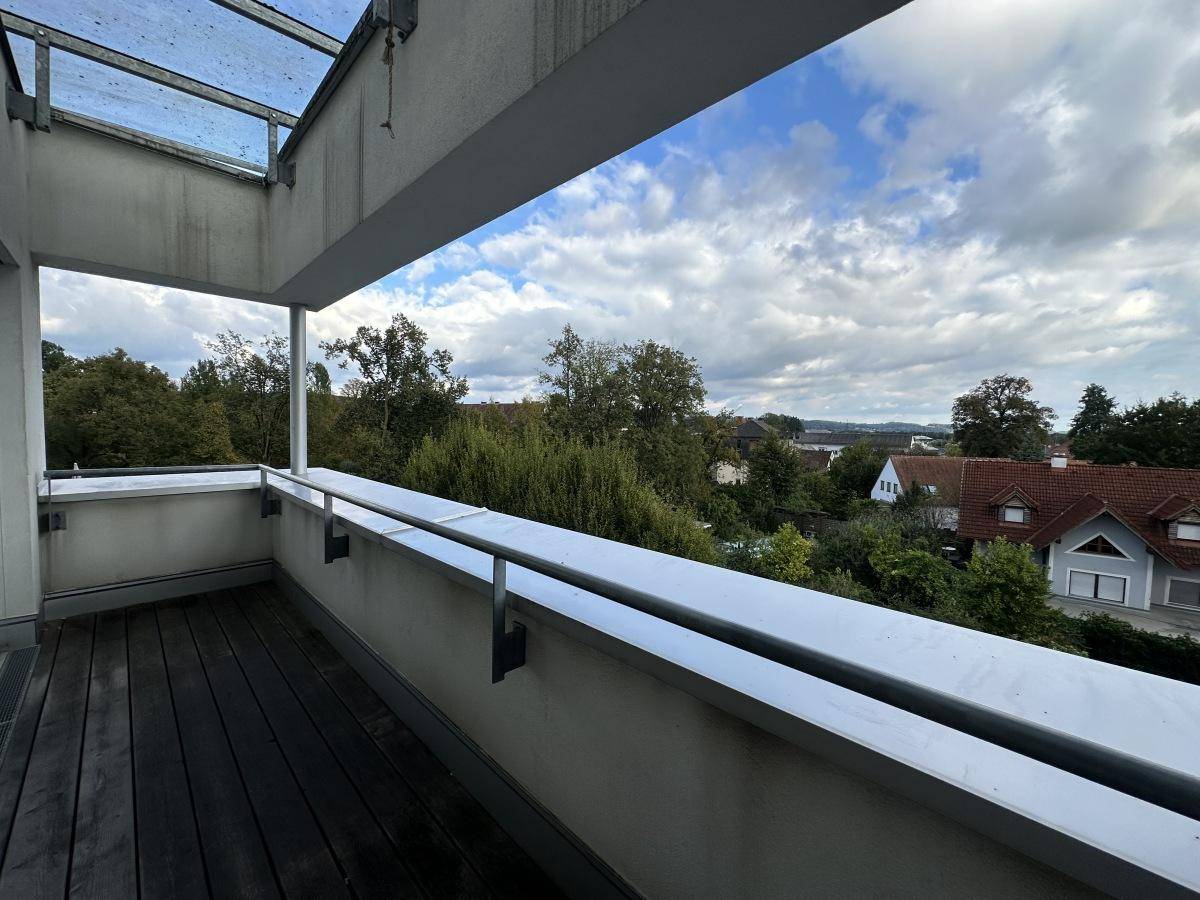 Balkon mit Holzboden und weitem Blick über grüne Bäume und die umliegende Wohngegend.