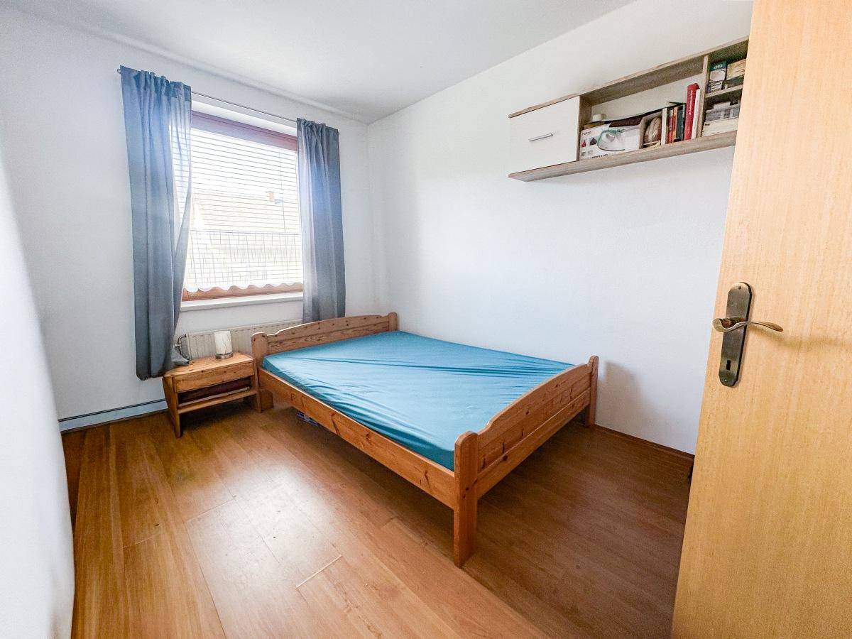 Schlafzimmer mit Holzbett, Wandregal und Laminatboden, ideal für Gäste.