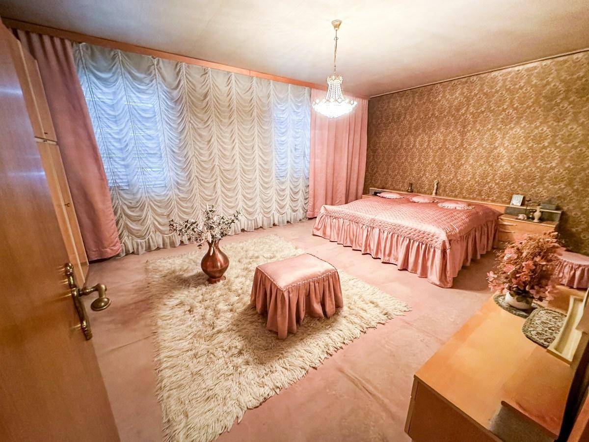 Geräumiges Schlafzimmer mit rosa Bett, Teppichboden und gemusterter Tapete.