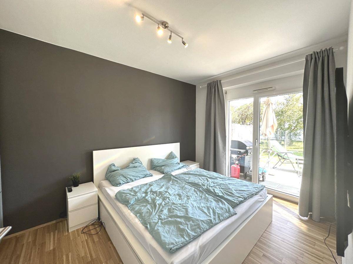 Schlafzimmer mit Doppelbett, dunkler Akzentwand und Zugang zur Terrasse.