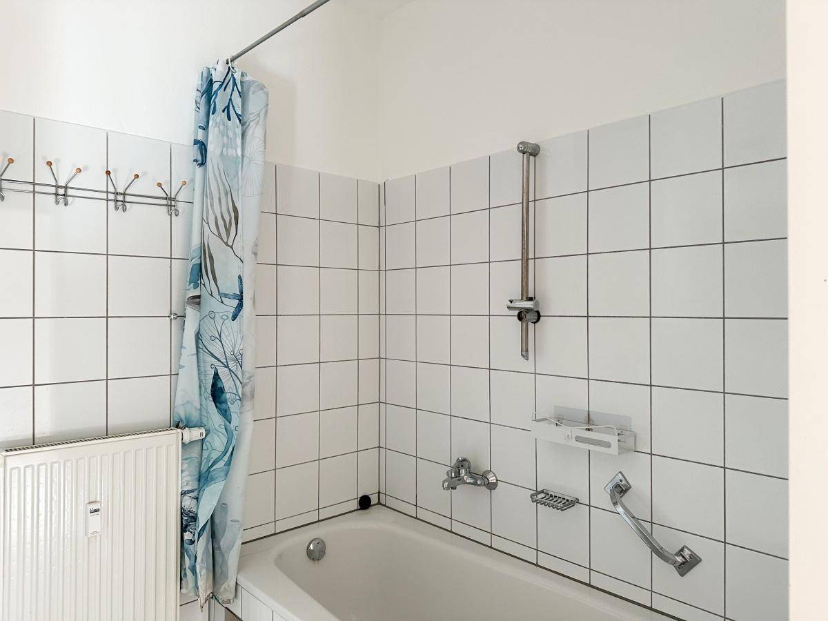 Badewanne mit Duschvorhang, Duschkopf und Haltegriff in einem gefliesten Badezimmer.