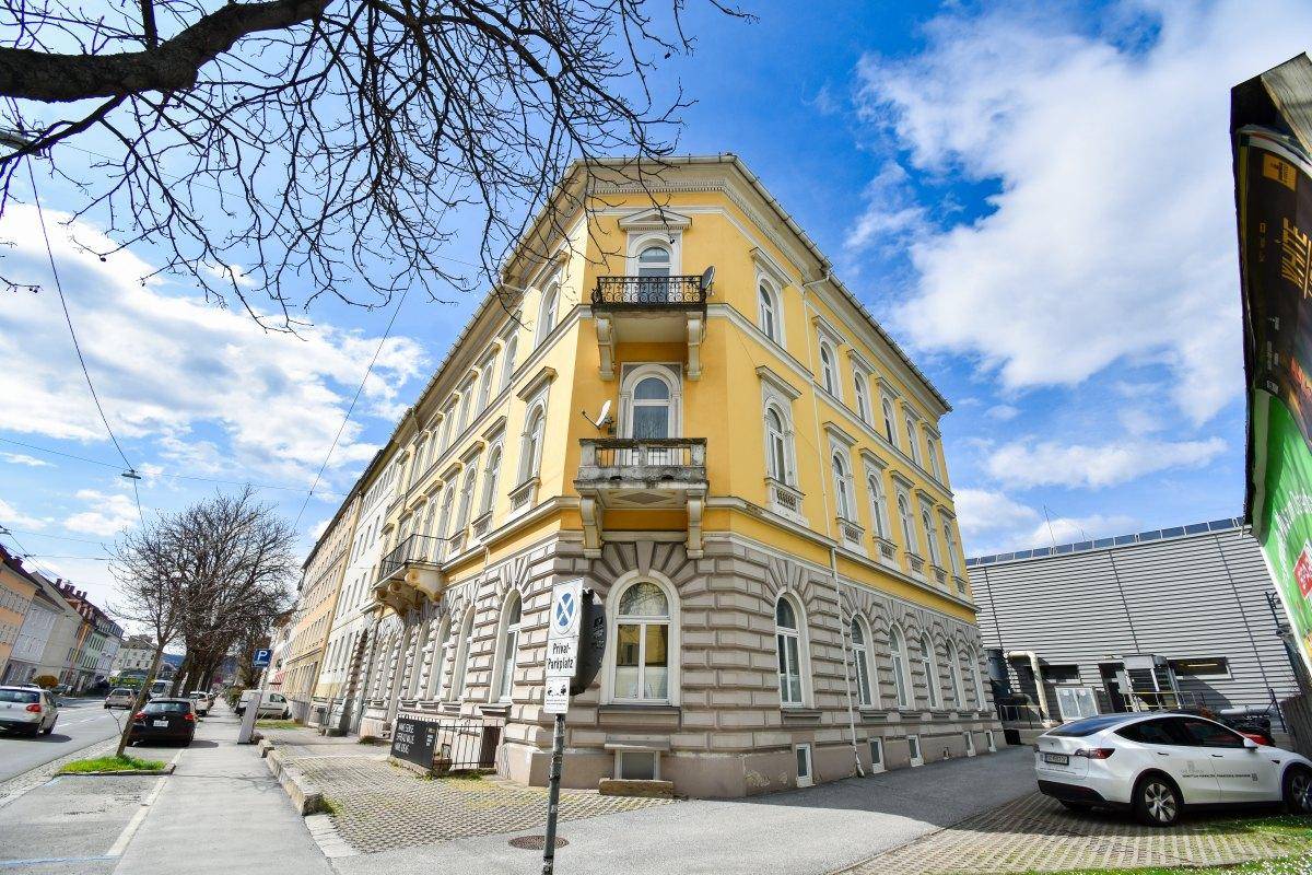 Eckansicht eines historischen Gebäudes mit gelber Fassade, dekorativen Balkonen und großen Fenstern.