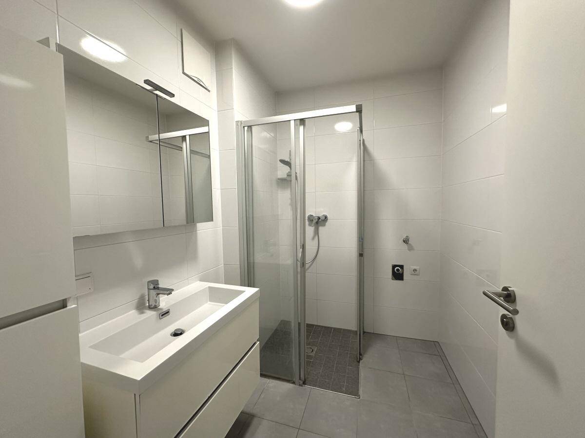 Modernes Badezimmer mit weißen Fliesen, Einzelwaschbecken und einer Duschkabine aus Glas.