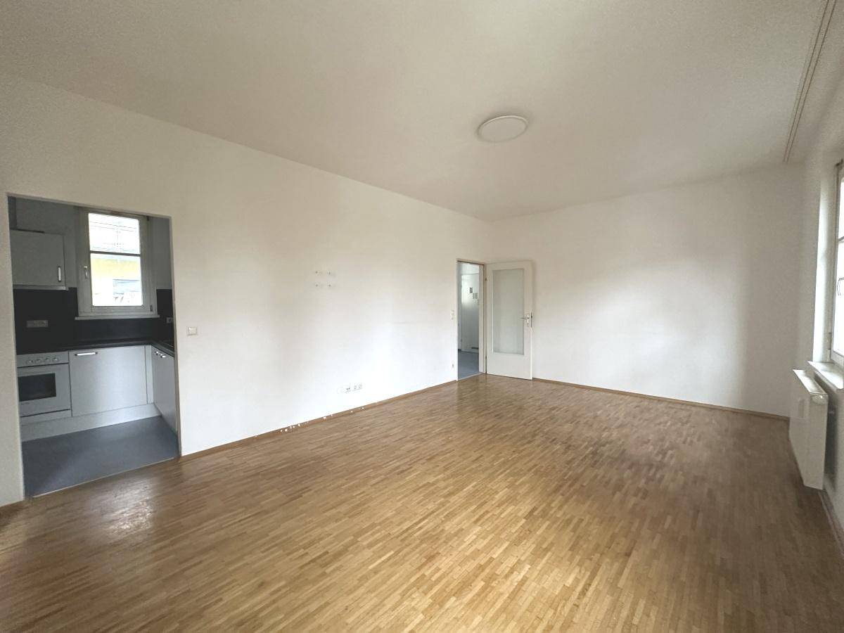 Heller Wohnbereich mit Parkettboden und offenem Zugang zu einer kleinen Küchenzeile.