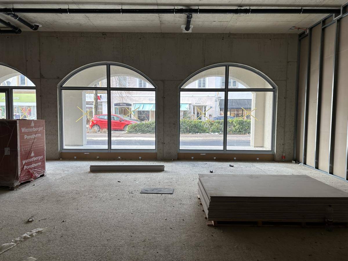 Rohbau eines Gewerberaums mit großen Bogenfenstern und gestapelten Trockenbauplatten, bereit für den Ausbau.