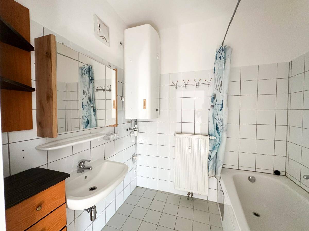 Badezimmer mit Badewanne, Waschbecken, weißen Fliesen und einem Warmwasserboiler.