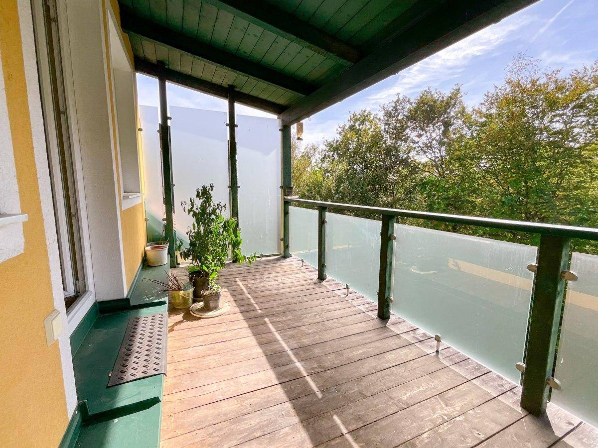 Geräumiger Balkon mit Holzboden und Blick ins Grüne.