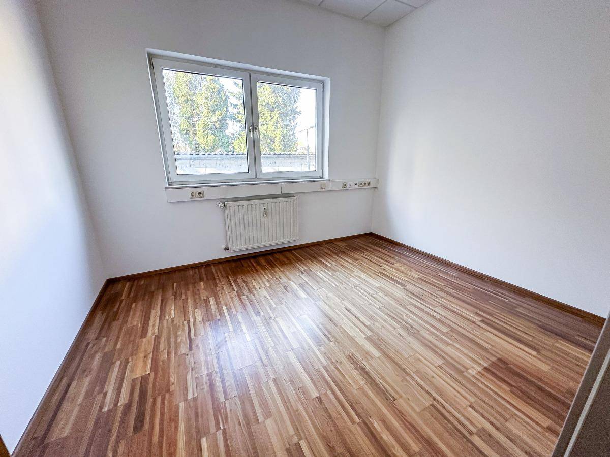 Heller Büroraum mit großen Fenstern, Holzboden und weißen Wänden.