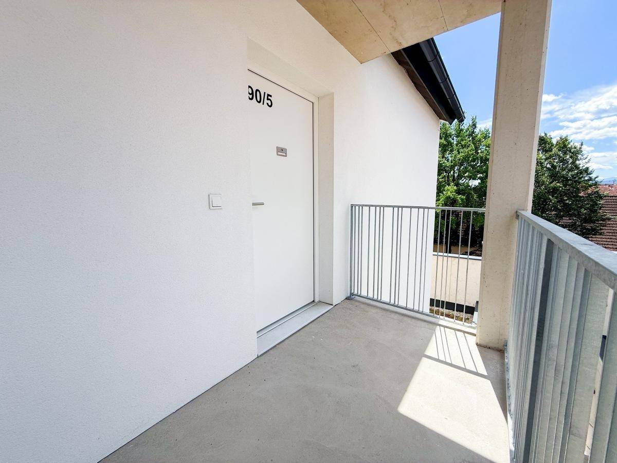 Kleiner Balkon vor der Wohnungstür mit Metallgeländer und Blick ins Grüne.