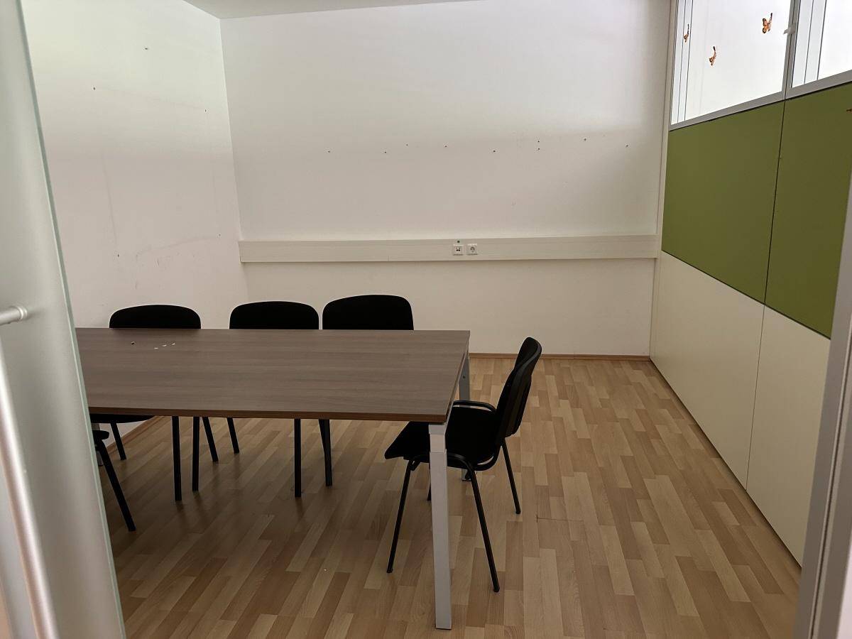 Besprechungsraum oder kleines Büro mit Tisch und Stühlen, Holzparkettboden und einem modernen Schrank.