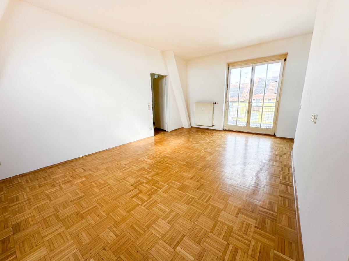 Geräumiges Wohnzimmer mit Parkettboden und großen Fenstern, die zu einem französischen Balkon führen.