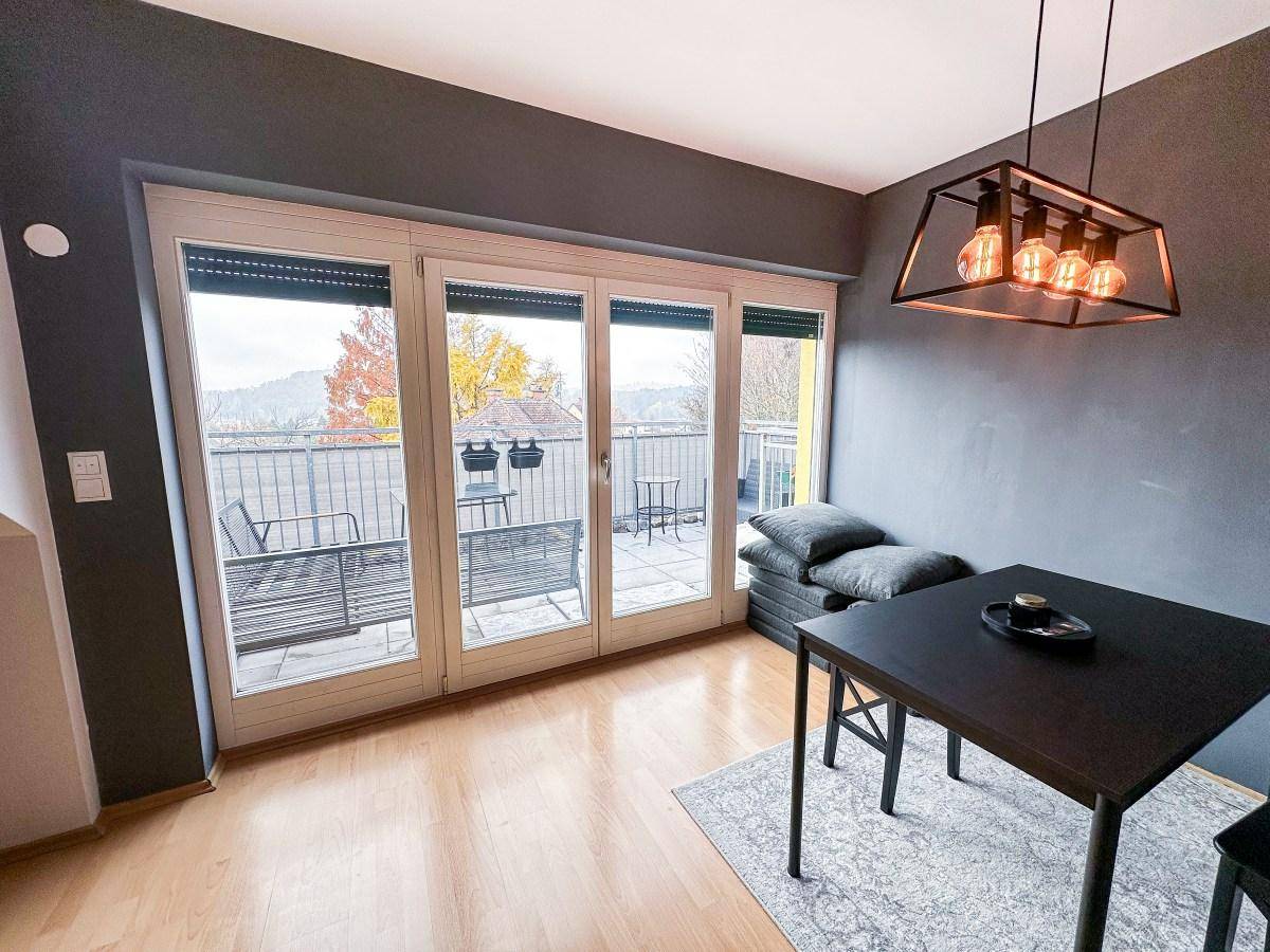 Essbereich mit dunklem Tisch, moderner Pendelleuchte und Zugang zum Balkon.