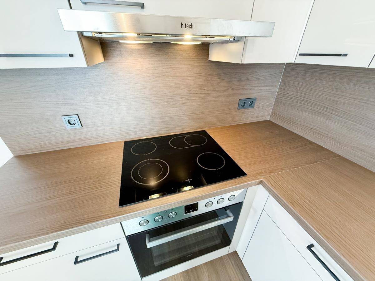 Kochbereich in einer modernen Küche mit Glaskeramikkochfeld, Backofen und Dunstabzugshaube.