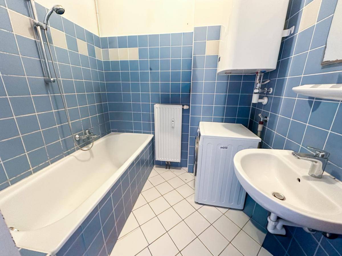 Badezimmer mit blauen Fliesen, Badewanne mit Duschfunktion und Waschbecken.