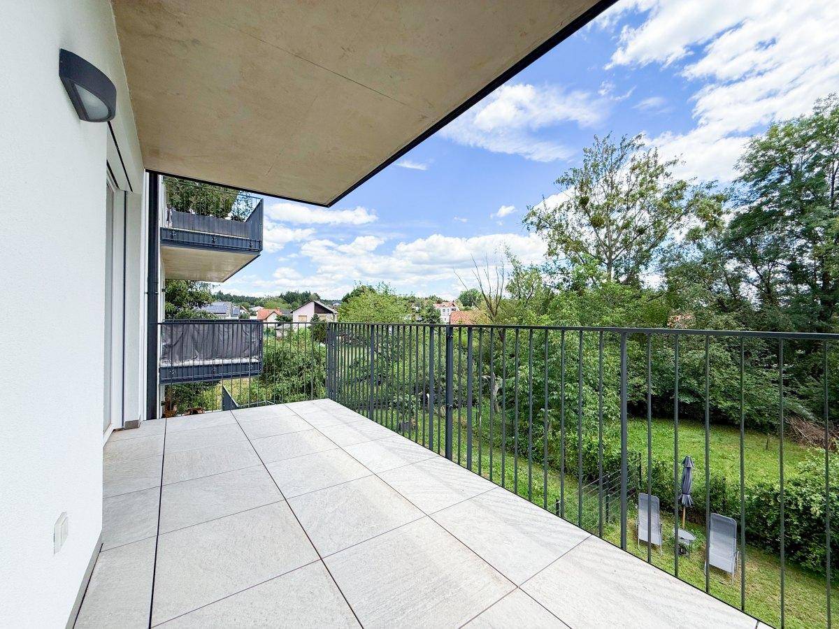 Geräumiger Balkon mit Fliesenboden und Metallgeländer, bietet einen weiten Blick ins Grüne.