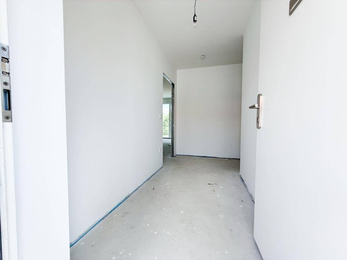 Eingangsbereich im Rohbau mit weiß gestrichenen Wänden und provisorischer Beleuchtung.