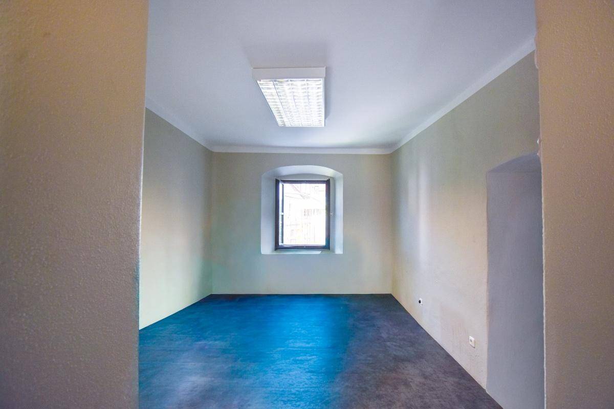 Leerer Raum mit dunklem Bodenbelag und einem kleinen Fenster, bereit zur individuellen Gestaltung.