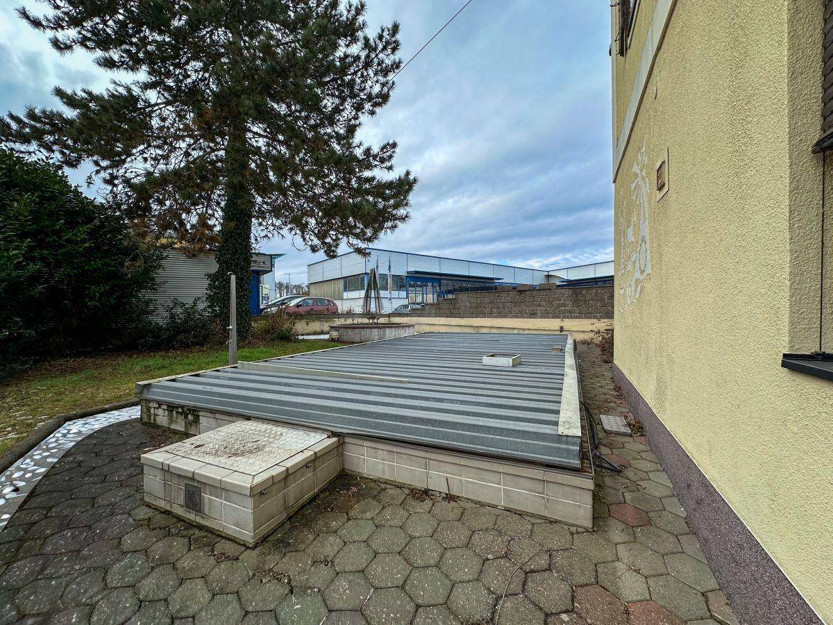 Außenbereich des Hauses mit überdachtem Pool und gepflastertem Weg.