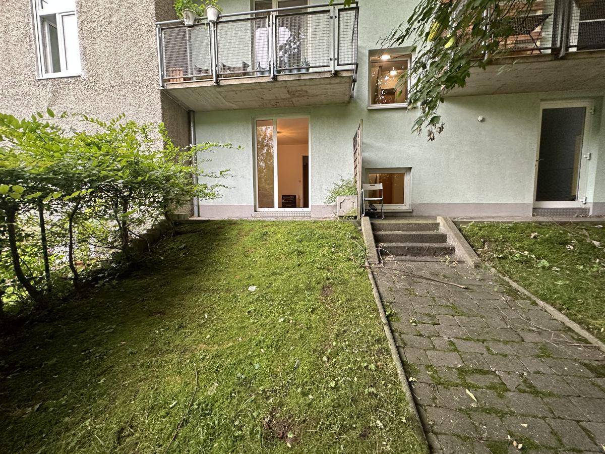Außenansicht des Gebäudes mit Rasenfläche, gepflastertem Weg und Zugang zum Garten.