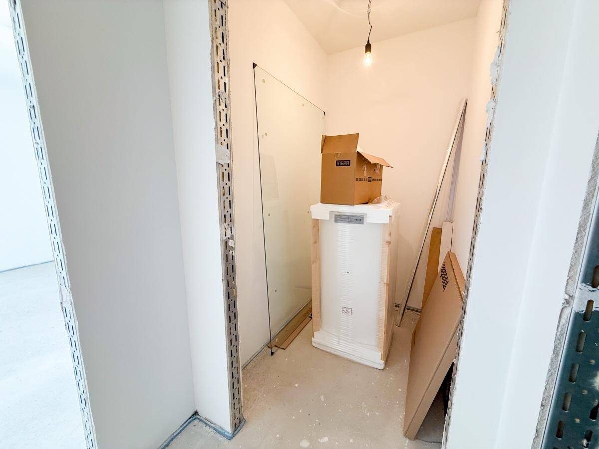 Kleiner Raum im Rohbau mit einer Glaswand, möglicherweise für eine Dusche, und Baumaterialien.