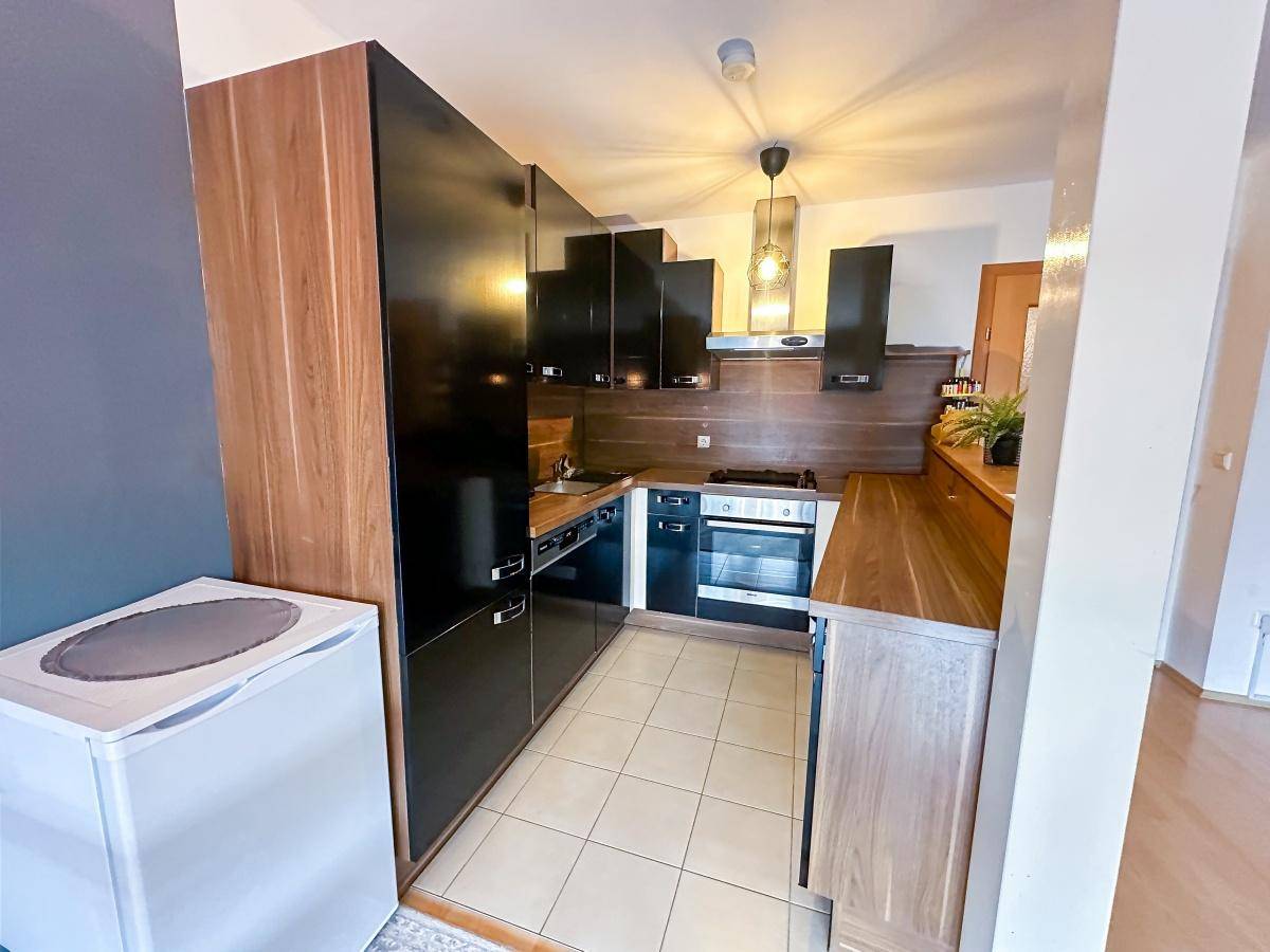 Funktionale Küche mit schwarzen Hochglanzfronten, Holzakzenten und integrierten Geräten.