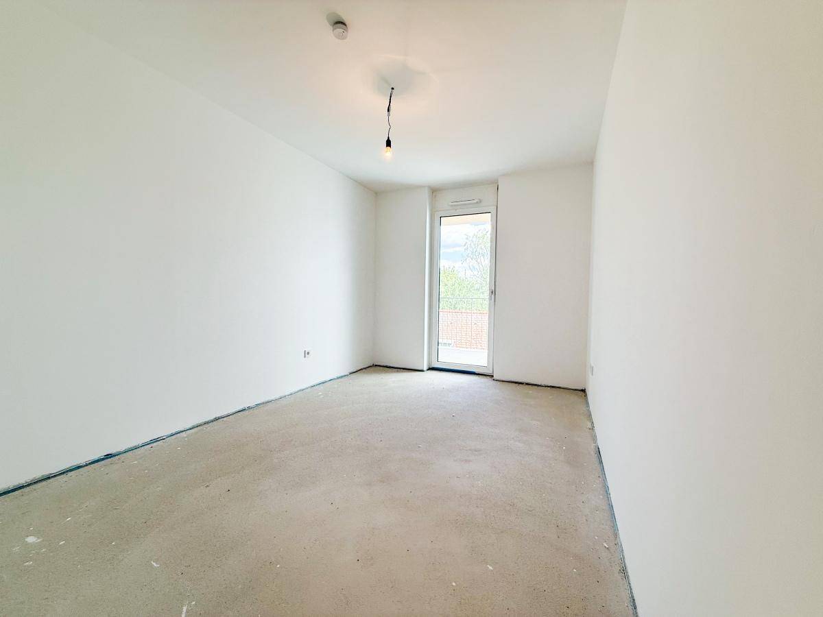 Leeres Zimmer im Rohbau mit Zugang zu einem Außenbereich und heller Atmosphäre.
