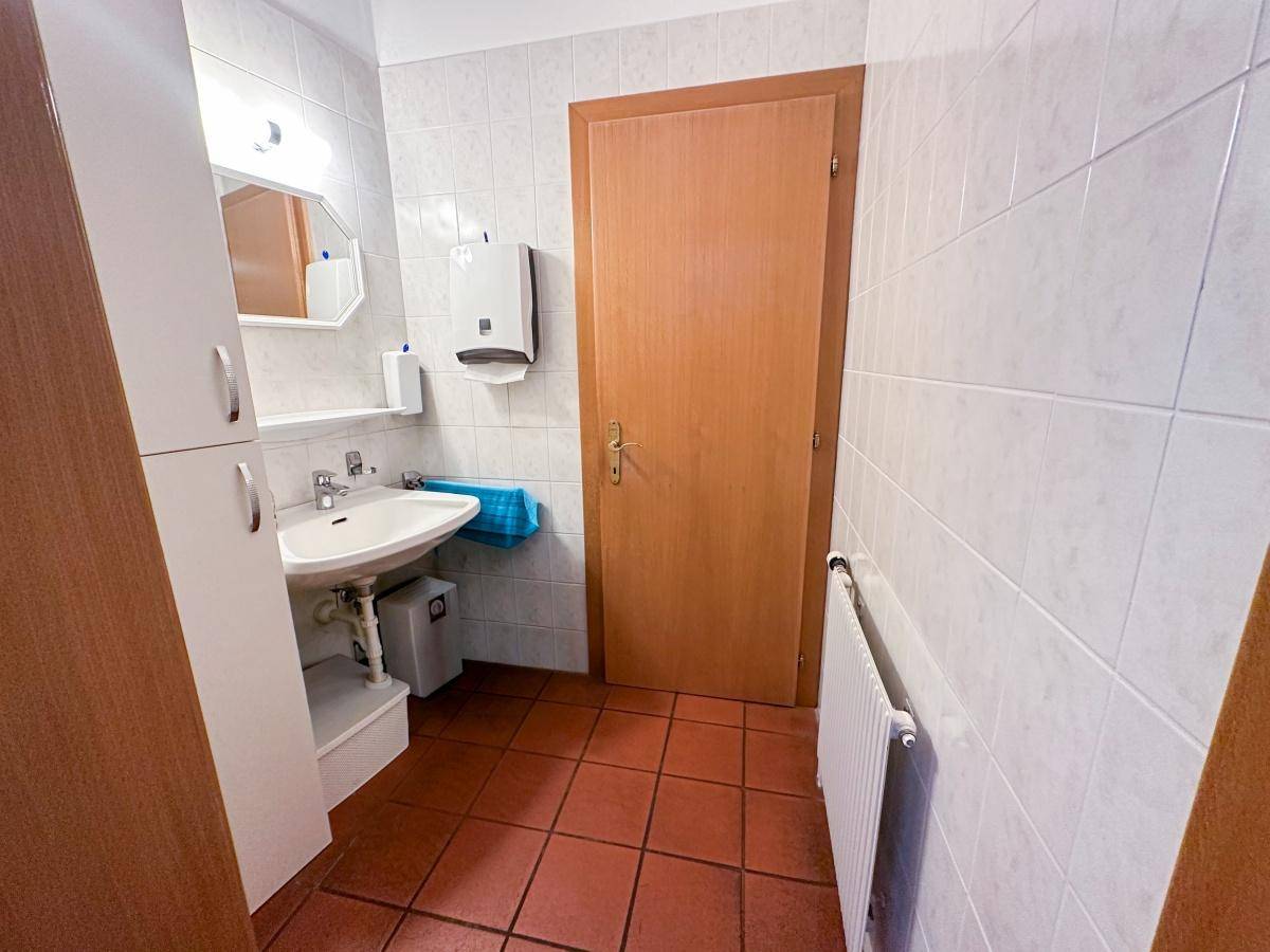 Badezimmer mit Waschbecken, Spiegel, weißen Fliesen und Terrakotta-Bodenfliesen.