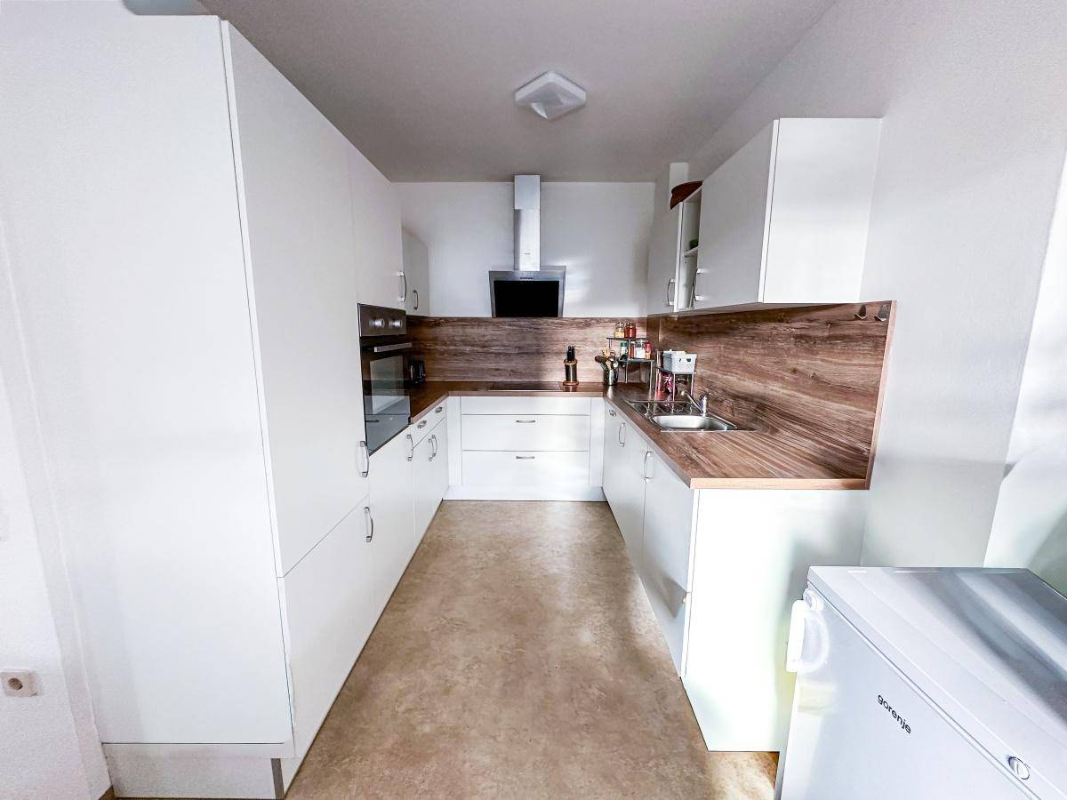 Helle Einbauküche mit weißen Fronten, Holzoptik-Arbeitsplatten und modernen Geräten.