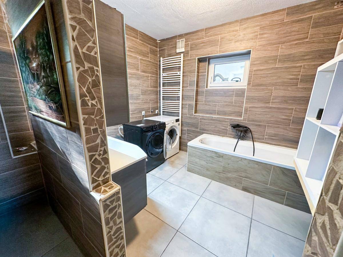 Geräumiges Badezimmer mit Badewanne, Waschmaschine und Trockner sowie beheiztem Handtuchhalter.