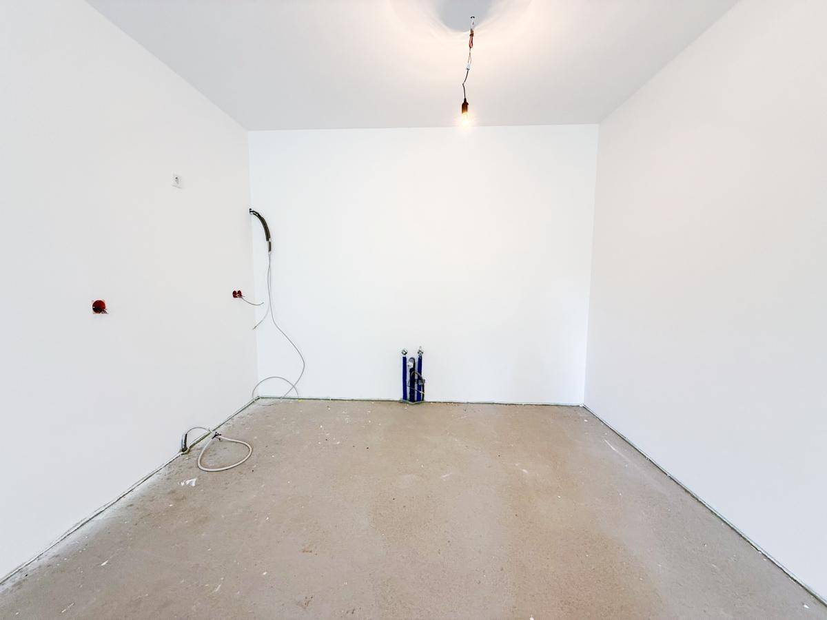 Rohbau-Raum mit weißen Wänden und sichtbaren Installationen für zukünftige Küchen- oder Badnutzung.