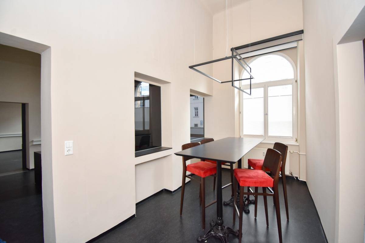 Essbereich mit Stehtisch und roten Stühlen, beleuchtet durch ein großes Bogenfenster, ideal für Pausen.