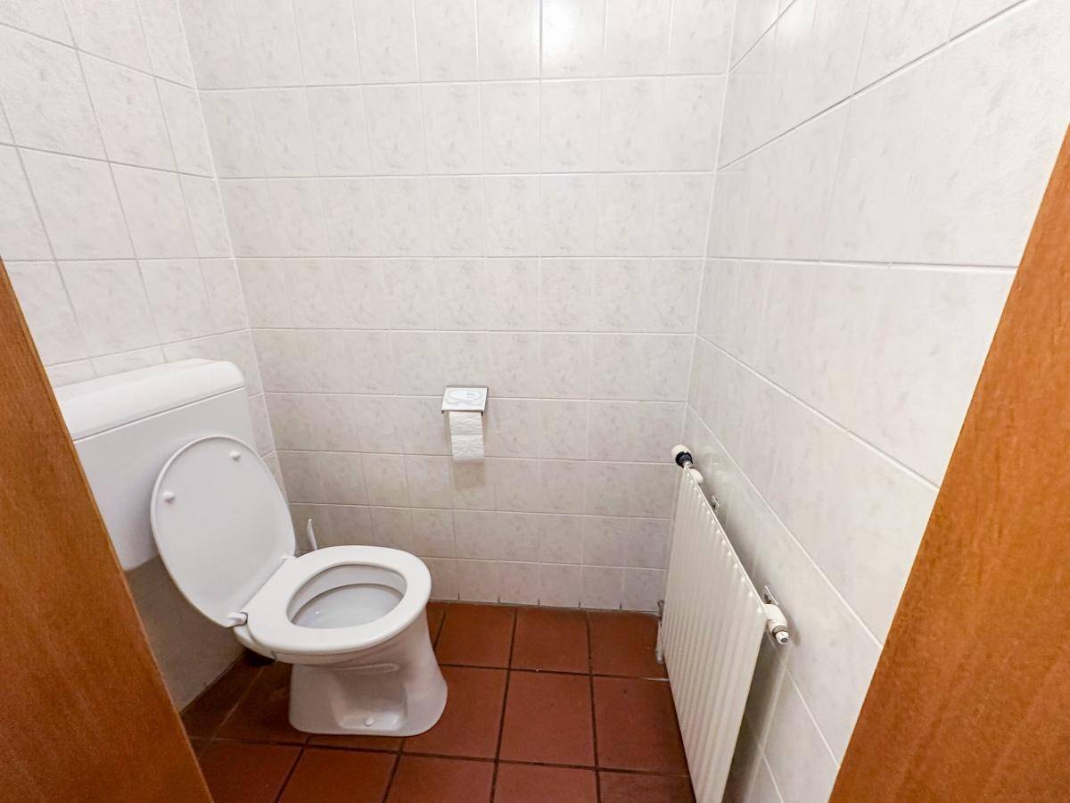 Separate Toilette mit weißen Wandfliesen, Terrakotta-Bodenfliesen und Heizkörper.