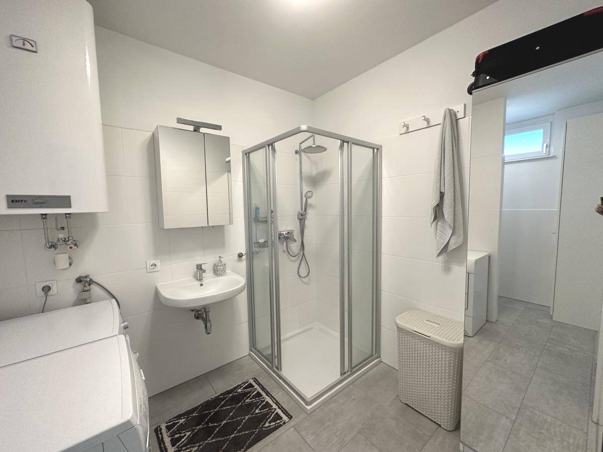 Modernes Badezimmer mit Duschkabine, Waschbecken und Waschmaschinenanschluss.