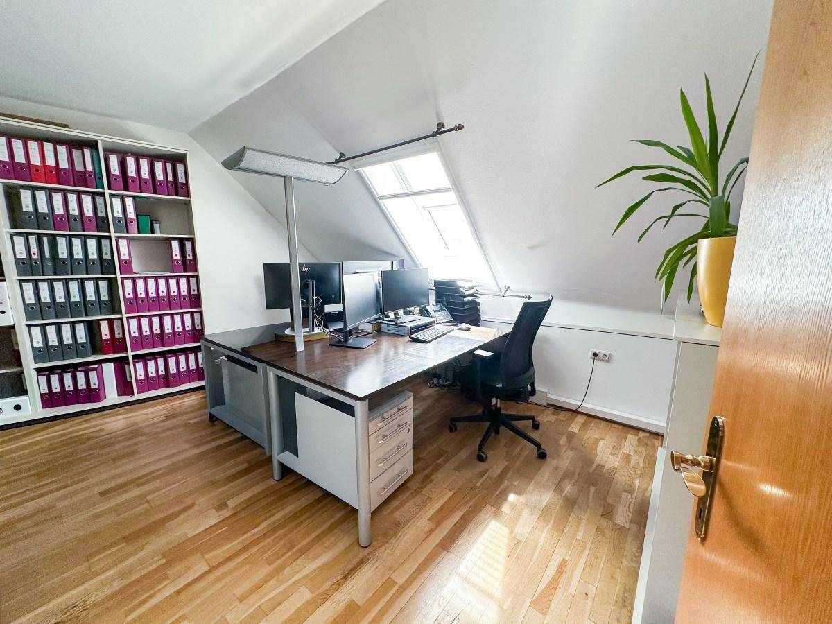 Detailansicht eines Arbeitsplatzes im Dachgeschossbüro mit Computern, Schreibtisch und Aktenregal.