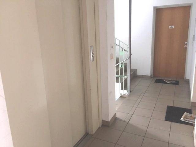 Heller Flur mit Fliesenboden, Aufzug und Treppenhauszugang im Mehrfamilienhaus.