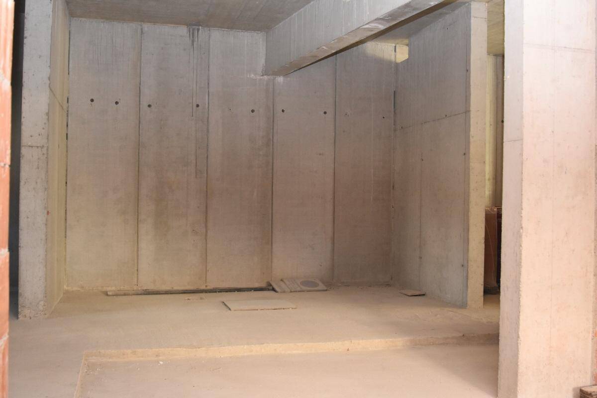 Unfertiger Raum mit hohen Betonwänden und einem markanten Betonbalken, der die Decke stützt.