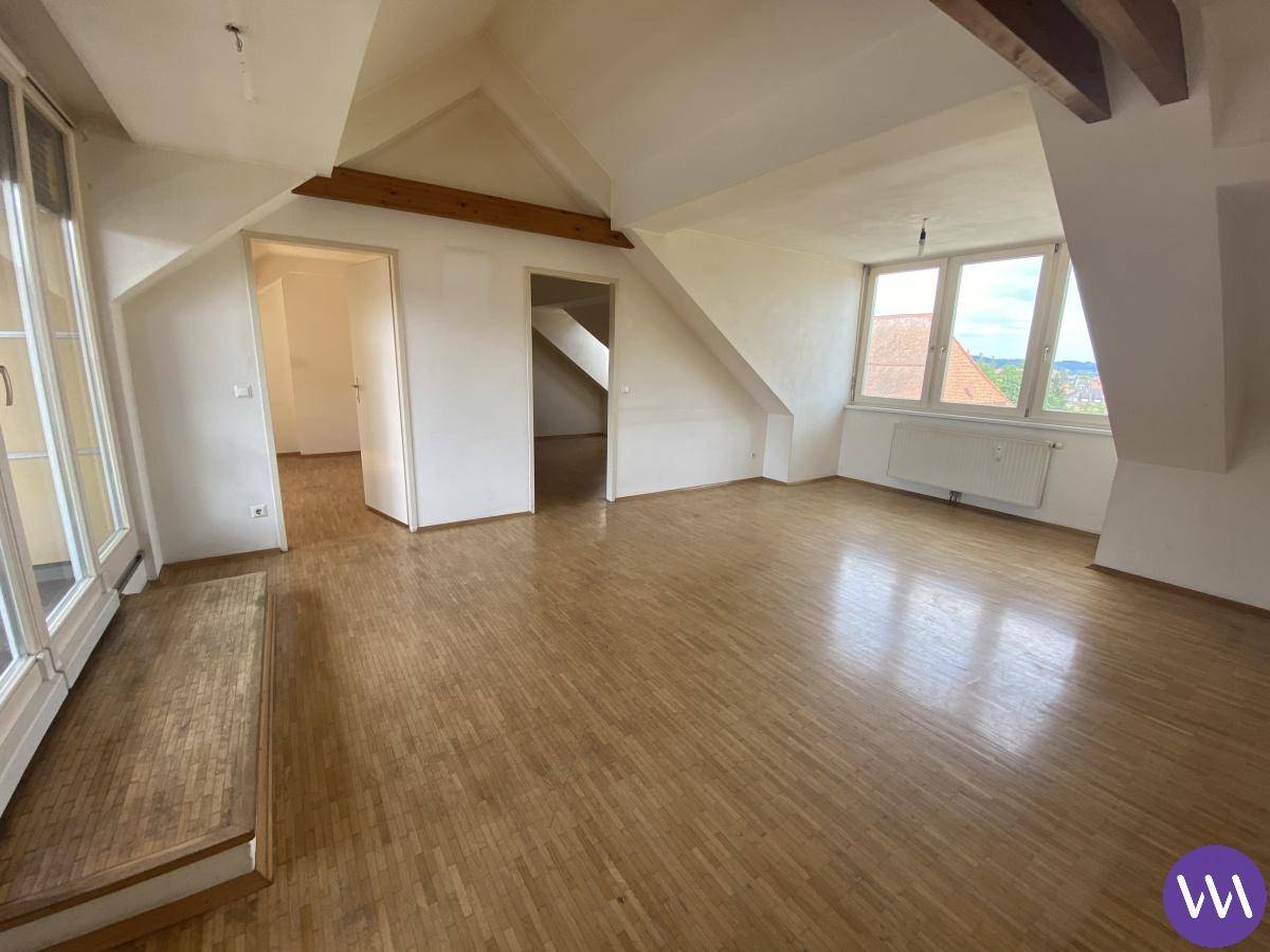 Helles und geräumiges Wohnzimmer im Dachgeschoss mit Holzbalken und Parkettboden.
