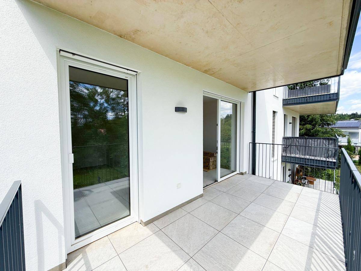 Heller Balkon mit Fliesenboden und großen Glastüren, die den Zugang zum Innenbereich ermöglichen.