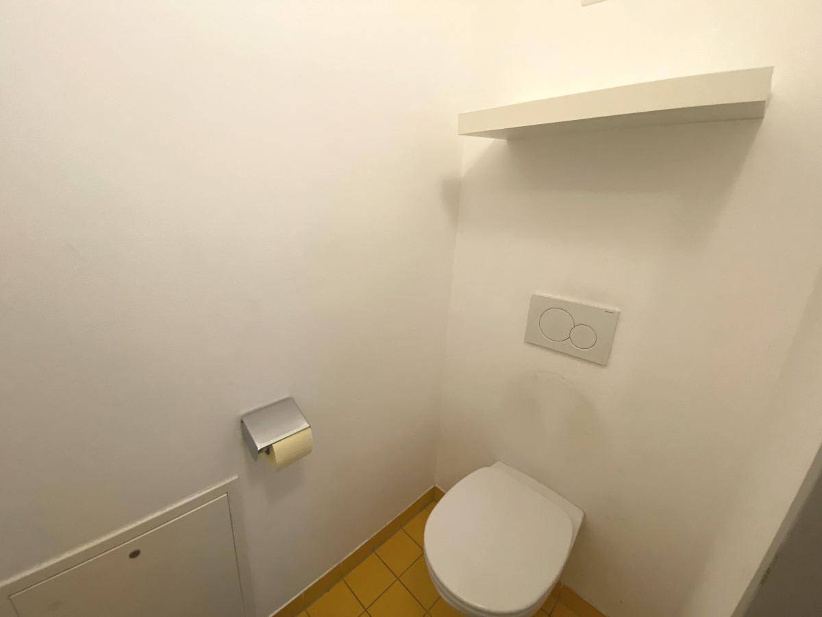 Separates WC mit wandhängender Toilette und gelben Bodenfliesen.