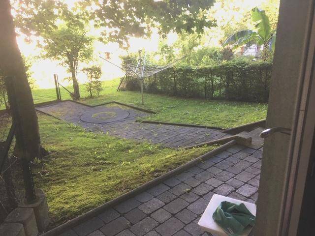 Ruhiger Gartenbereich mit gepflasterter Fläche, Rasen und üppiger Bepflanzung.
