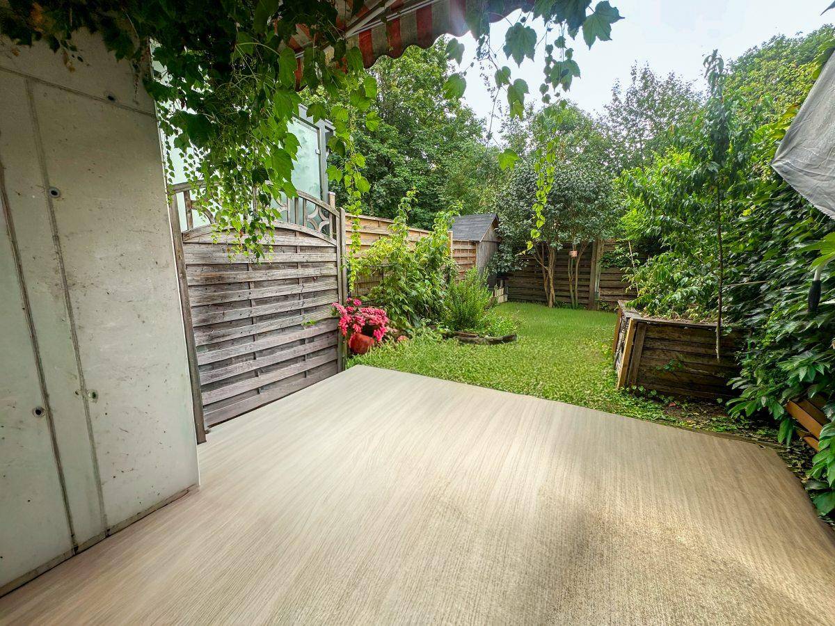 Grüner Gartenbereich mit Rasenfläche, Holzzaun und einer gepflasterten Terrasse.